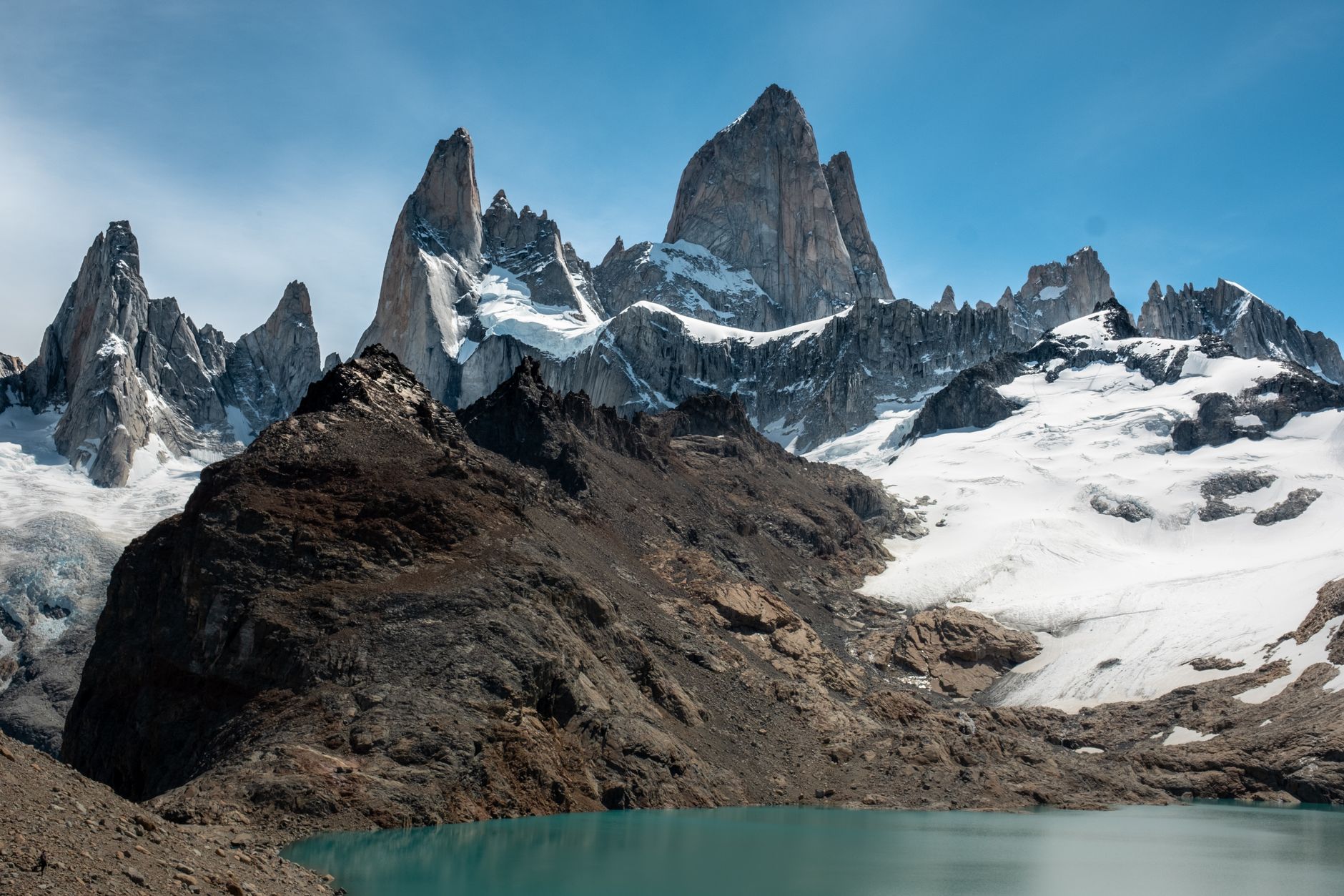 Massive glacier calving into teal water with mountain backdrop